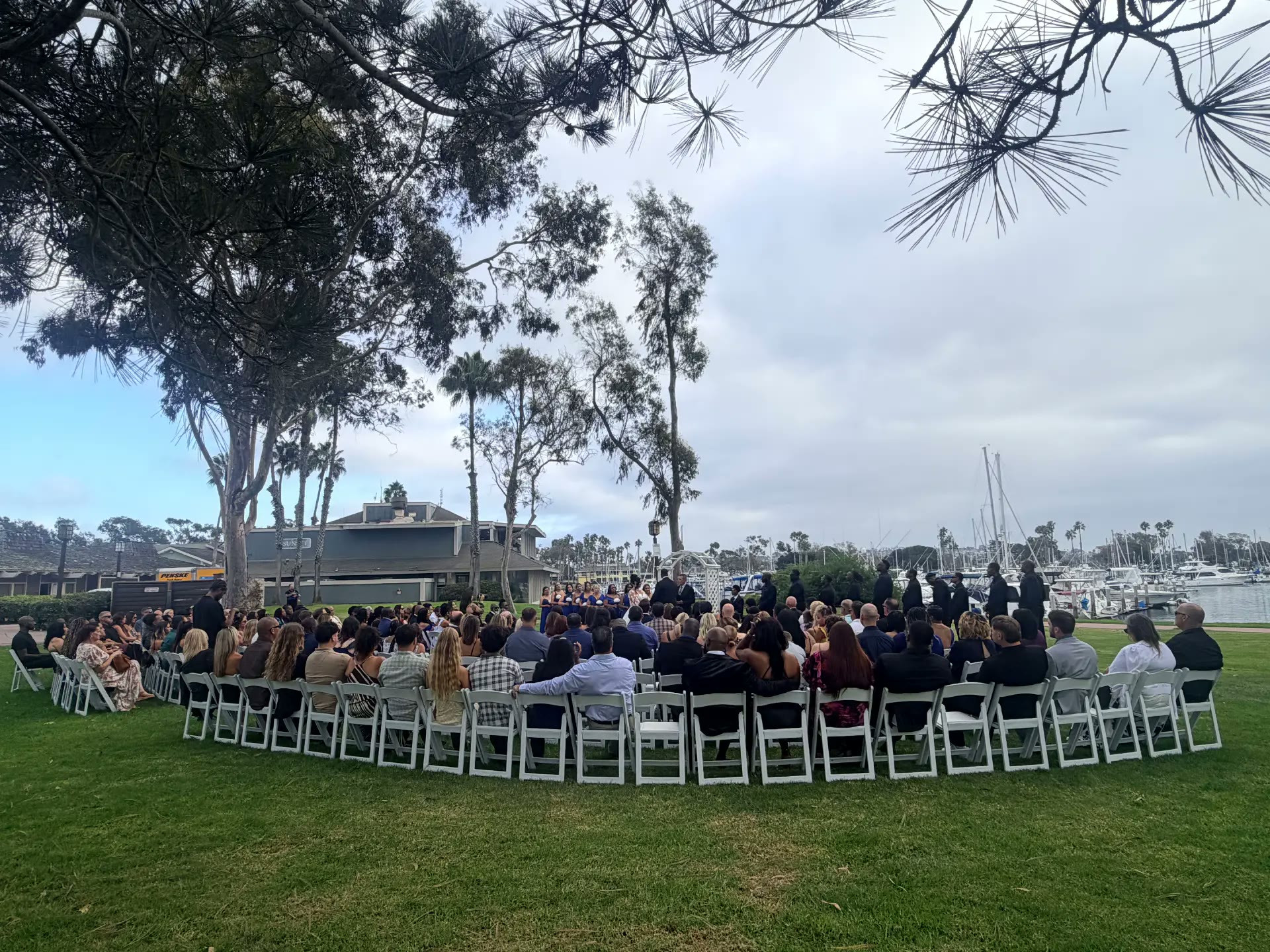Waterside wedding ceremony with white chairs beneath towering trees