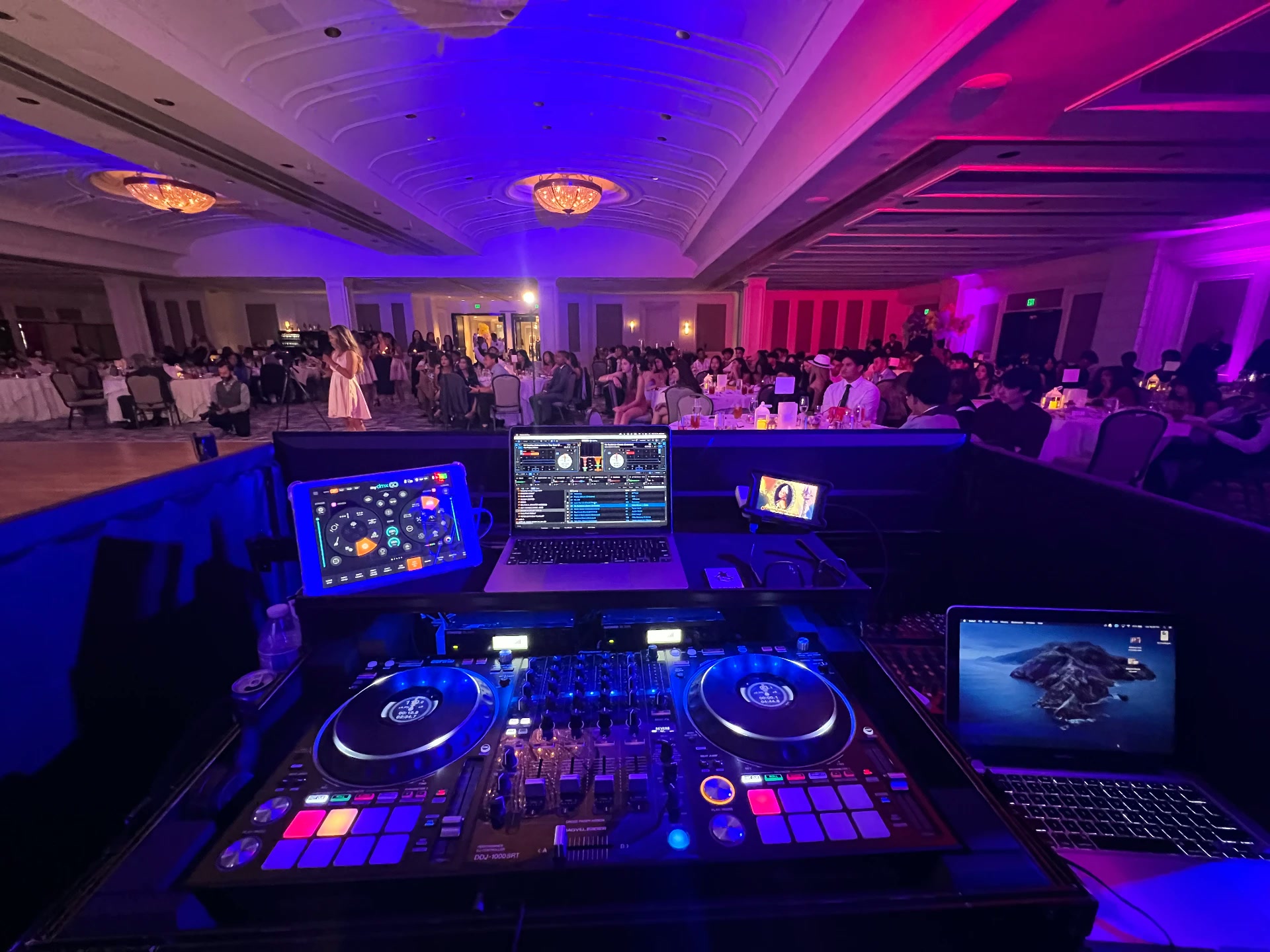 Grand ballroom dance floor washed in pink and blue lighting with dual DJ decks